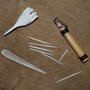 Tools, clockwise from lower left: large awl, sewing awl, rivercane needle case, bone toothpick, sewing needles in center.